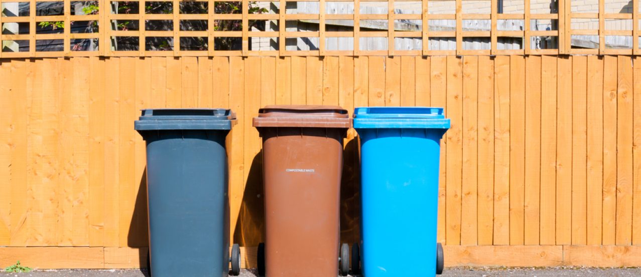 Three plastic waste bins outside a house along the fence