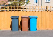 Opłata śmieciowa od zużycia wody w kolejnym dużym mieście Three plastic waste bins outside a house along the fence