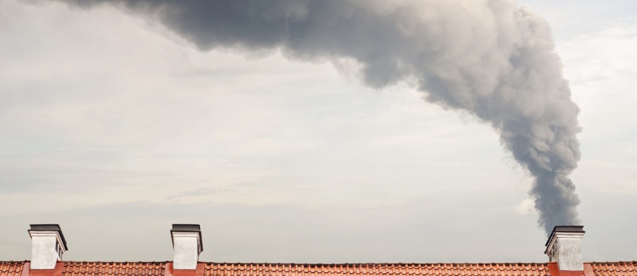 Huge dark smoke raising from a chimney, tiled brown roof